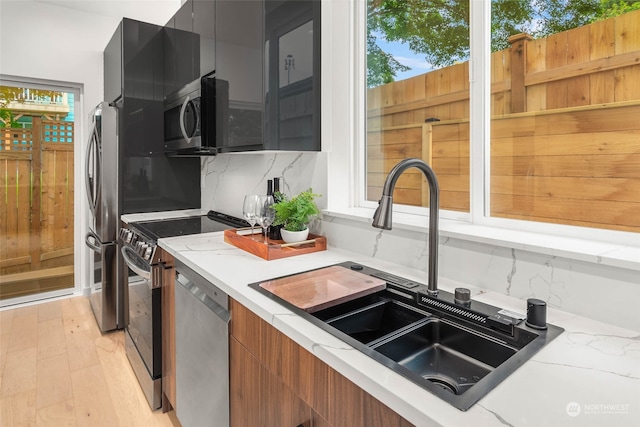 kitchen with decorative backsplash, light hardwood / wood-style flooring, sink, appliances with stainless steel finishes, and light stone counters