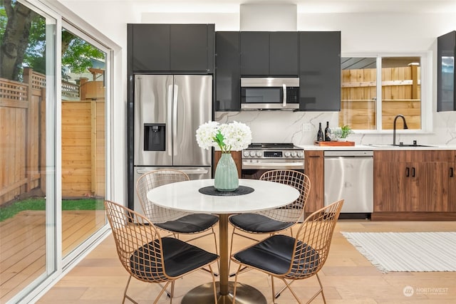 kitchen with appliances with stainless steel finishes, decorative backsplash, sink, and light hardwood / wood-style floors