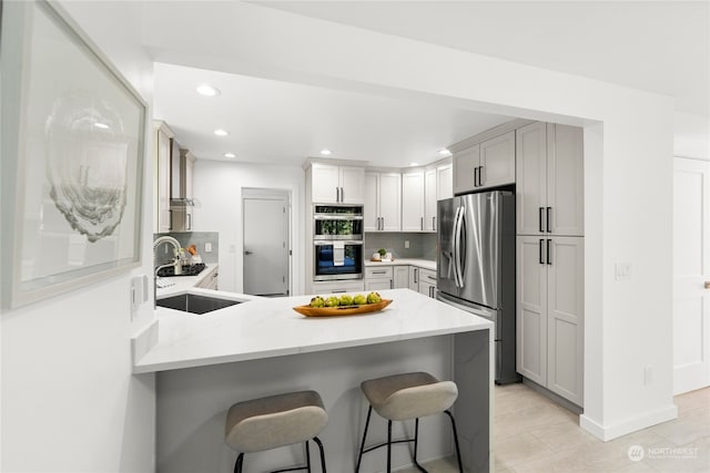 kitchen featuring appliances with stainless steel finishes, a kitchen breakfast bar, tasteful backsplash, kitchen peninsula, and sink