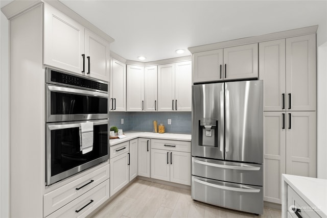 kitchen featuring light wood-type flooring, backsplash, white cabinetry, and stainless steel appliances