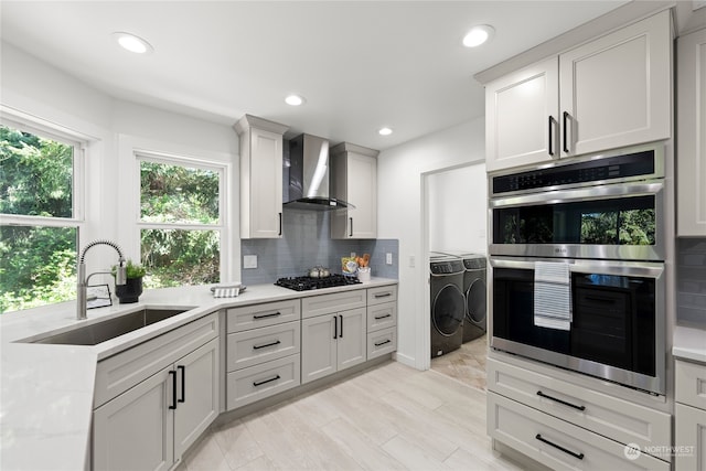 kitchen with white cabinets, sink, wall chimney range hood, washer and clothes dryer, and double oven