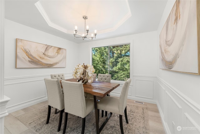 dining area featuring light hardwood / wood-style flooring, a chandelier, a raised ceiling, and crown molding