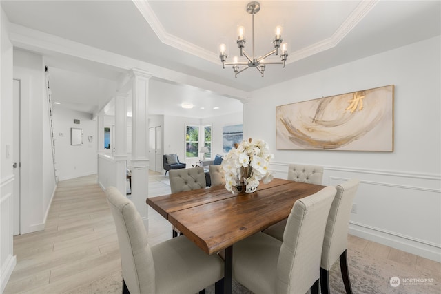 dining area with light wood-type flooring, a raised ceiling, ornamental molding, and ornate columns