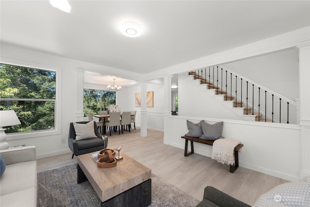 living room with decorative columns, light hardwood / wood-style floors, and a chandelier