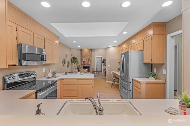 kitchen with light wood-type flooring, sink, light brown cabinets, appliances with stainless steel finishes, and a large fireplace