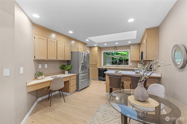 kitchen with appliances with stainless steel finishes, light brown cabinets, a kitchen bar, light hardwood / wood-style flooring, and a skylight