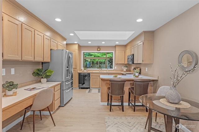 kitchen with light brown cabinets, a skylight, stainless steel appliances, light wood-type flooring, and a kitchen bar