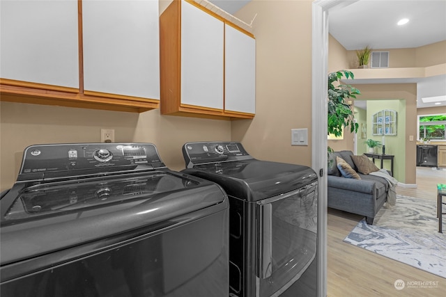 clothes washing area featuring light hardwood / wood-style flooring, cabinets, and separate washer and dryer