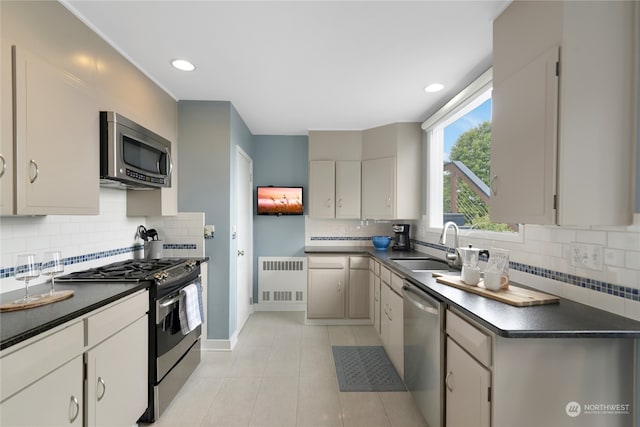 kitchen with tasteful backsplash, sink, stainless steel appliances, radiator, and light tile patterned floors