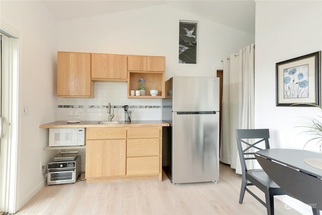 kitchen with stainless steel fridge, vaulted ceiling, light brown cabinetry, and light hardwood / wood-style flooring