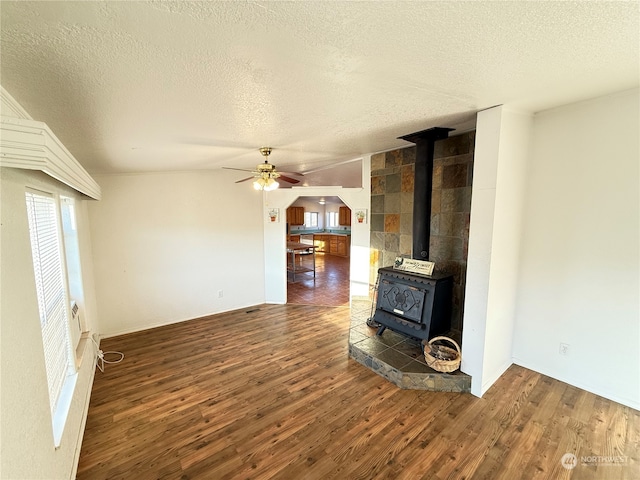 unfurnished living room featuring a textured ceiling, ceiling fan, dark wood-type flooring, and a wood stove