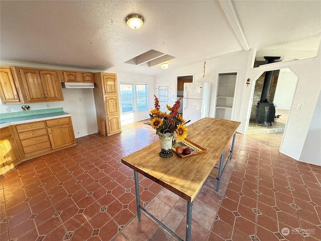 kitchen featuring dark tile patterned flooring, white refrigerator, a textured ceiling, a wood stove, and vaulted ceiling with beams