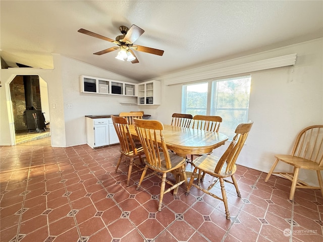 dining room featuring a textured ceiling, vaulted ceiling, ceiling fan, and a wood stove