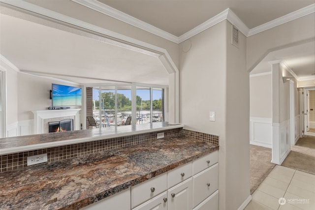 kitchen with dark stone counters, ornamental molding, white cabinetry, and light carpet