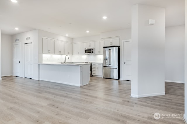 kitchen featuring sink, decorative backsplash, light wood-type flooring, white cabinetry, and stainless steel appliances