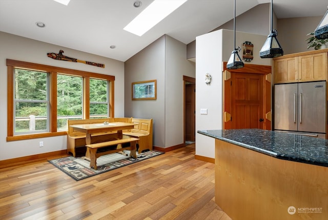 kitchen featuring lofted ceiling, decorative light fixtures, dark stone countertops, light hardwood / wood-style floors, and high end refrigerator