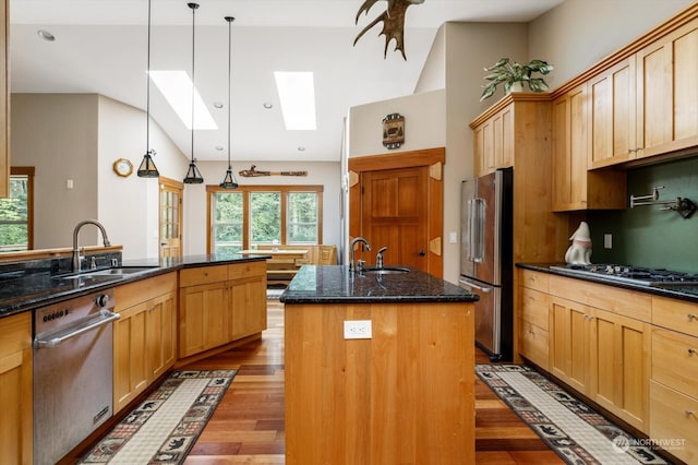 kitchen featuring hanging light fixtures, dark wood-type flooring, stainless steel appliances, a center island with sink, and sink