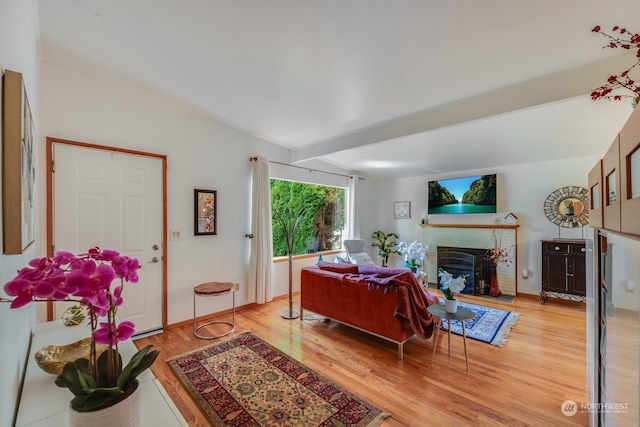 living room featuring beamed ceiling, light hardwood / wood-style floors, and a brick fireplace