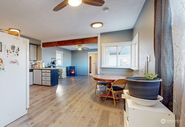 kitchen featuring ceiling fan, white refrigerator, a wood stove, light hardwood / wood-style floors, and beamed ceiling