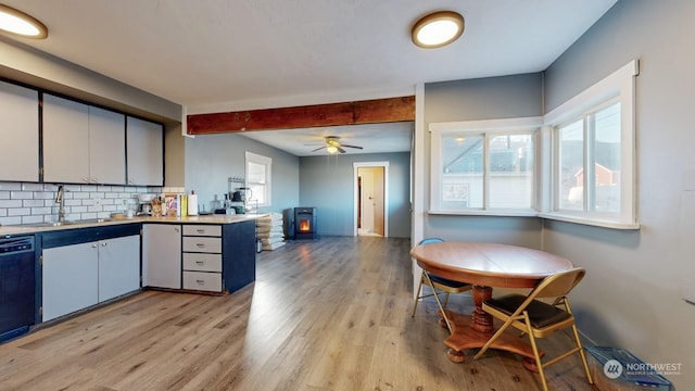 kitchen featuring dishwasher, decorative backsplash, sink, a wood stove, and light hardwood / wood-style flooring