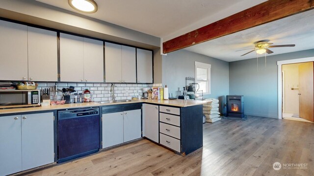 kitchen with black dishwasher, a wood stove, backsplash, sink, and light wood-type flooring