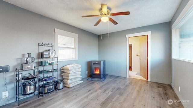 misc room with ceiling fan, plenty of natural light, light wood-type flooring, and a wood stove