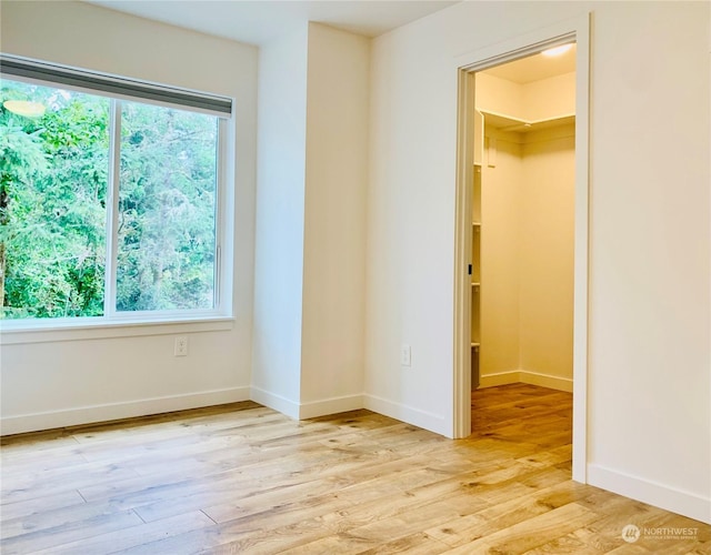 unfurnished bedroom featuring a walk in closet, a closet, light wood finished floors, and baseboards