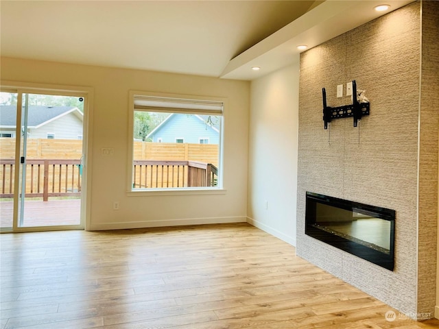 unfurnished living room featuring baseboards, wood finished floors, a large fireplace, and recessed lighting