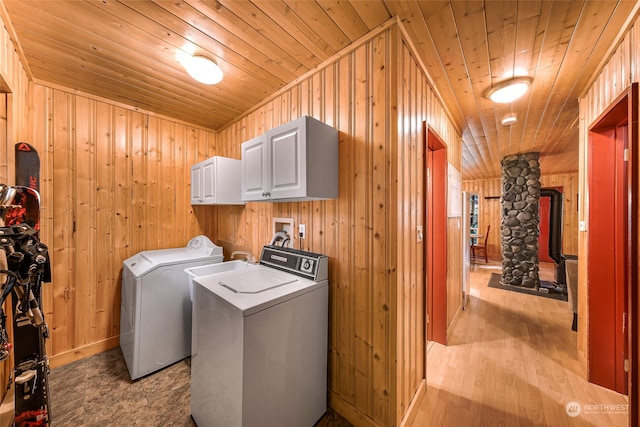 clothes washing area with wood ceiling, separate washer and dryer, wood walls, light hardwood / wood-style flooring, and cabinets