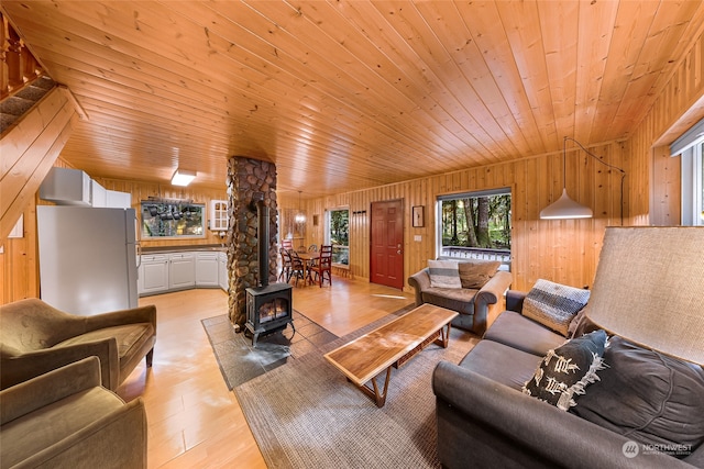 living room with wood walls, light hardwood / wood-style floors, a wood stove, and wooden ceiling