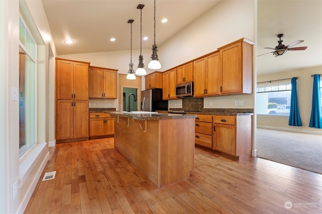 kitchen featuring a center island, stainless steel appliances, a breakfast bar, light carpet, and hanging light fixtures