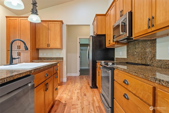 kitchen with light wood-type flooring, dark stone counters, sink, lofted ceiling, and appliances with stainless steel finishes