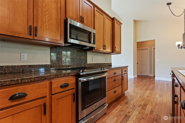 kitchen featuring an inviting chandelier, light hardwood / wood-style flooring, dark stone countertops, hanging light fixtures, and appliances with stainless steel finishes