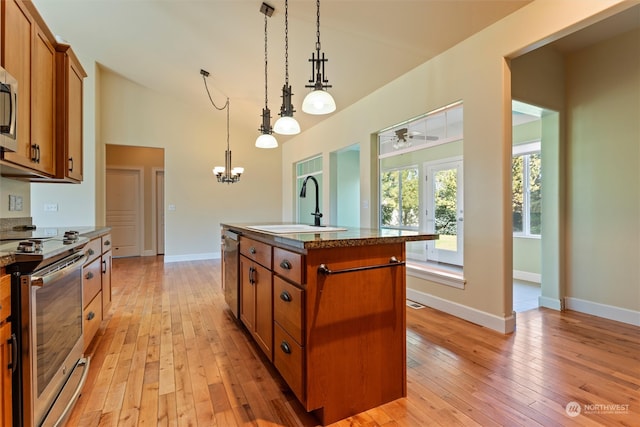 kitchen with light hardwood / wood-style floors, decorative light fixtures, a center island with sink, sink, and appliances with stainless steel finishes