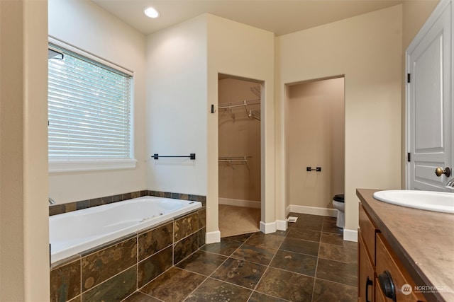 bathroom with vanity, tiled bath, and toilet