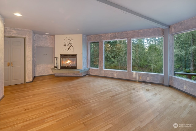 unfurnished living room featuring light hardwood / wood-style flooring, beamed ceiling, and a wealth of natural light