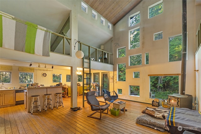 living room with wood ceiling, a wood stove, sink, high vaulted ceiling, and light hardwood / wood-style floors