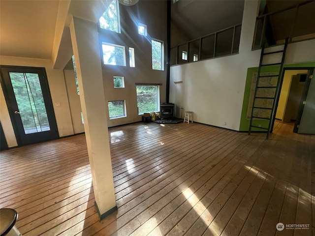 unfurnished living room featuring hardwood / wood-style flooring, a wood stove, and a high ceiling