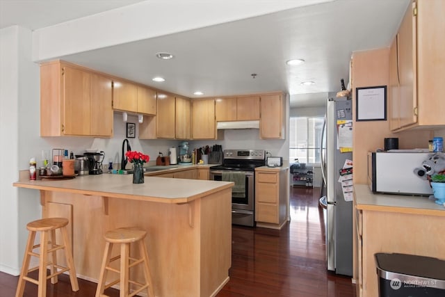 kitchen featuring dark hardwood / wood-style floors, kitchen peninsula, a kitchen bar, appliances with stainless steel finishes, and light brown cabinetry