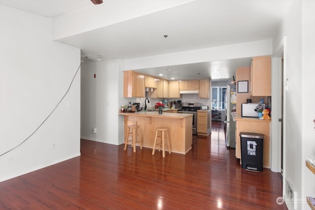 kitchen with kitchen peninsula, a kitchen breakfast bar, stainless steel appliances, light brown cabinetry, and dark hardwood / wood-style flooring