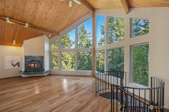 unfurnished sunroom featuring lofted ceiling with beams, ceiling fan, a tiled fireplace, and wooden ceiling