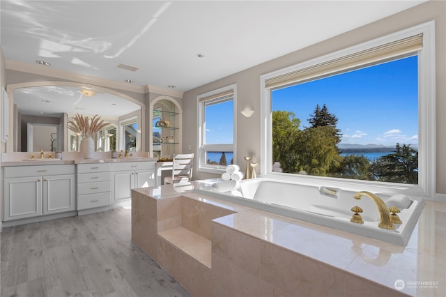 bathroom with a water view, tiled tub, vanity, crown molding, and hardwood / wood-style flooring