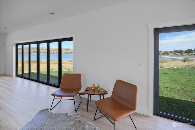 sitting room with a water view and light hardwood / wood-style flooring