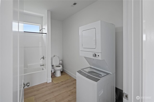 laundry area with stacked washer / dryer and light hardwood / wood-style flooring