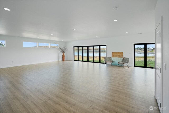 unfurnished living room with a wealth of natural light, light hardwood / wood-style flooring, and a water view