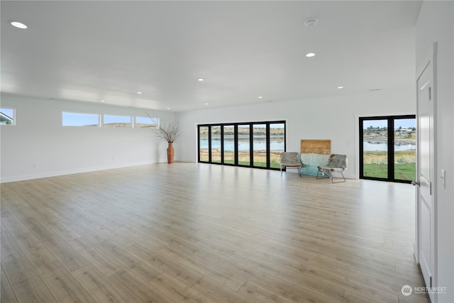 unfurnished living room featuring a healthy amount of sunlight, a water view, and light wood-type flooring