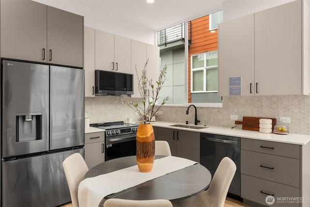 kitchen with gray cabinets, light countertops, backsplash, a sink, and stainless steel appliances