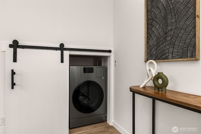 clothes washing area with washer / clothes dryer, a barn door, and wood finished floors