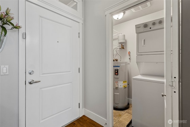 laundry room featuring stacked washer / dryer, tile patterned floors, and strapped water heater