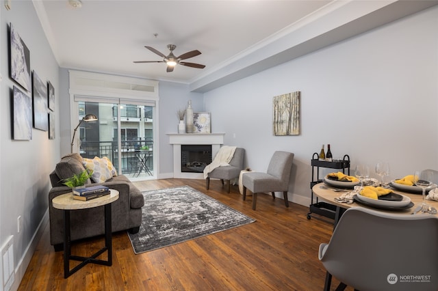 living room with ornamental molding, dark wood-type flooring, and ceiling fan